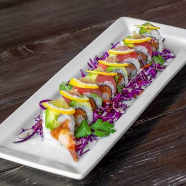 Sushi Omakase's colorful sushi roll with shrimp, avocado, tuna, and lemon slices on a white plate.