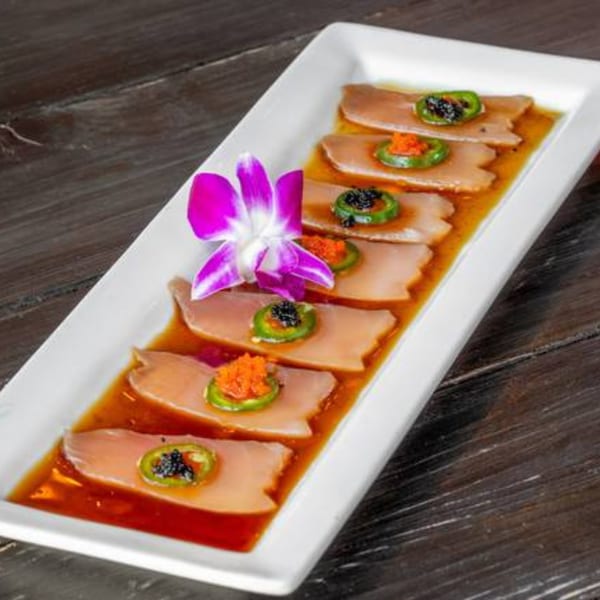 Sushi Omakase's tuna sashimi with jalapeño, caviar, and a purple orchid garnish on a white plate.