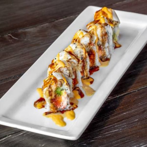 Sushi Omakase's sushi roll with creamy sauce and dark drizzle on a white rectangular plate.