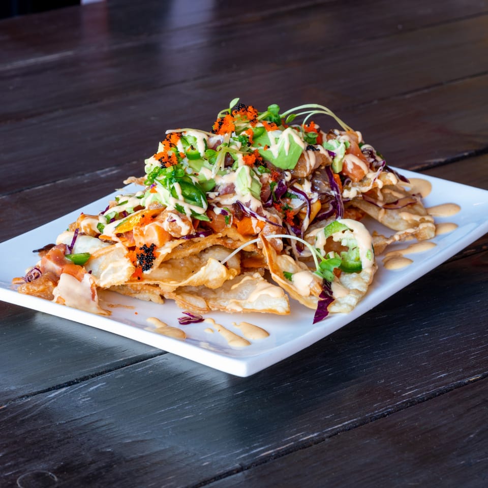 Sushi nachos with avocado, roe, and sauce on a white rectangular plate.