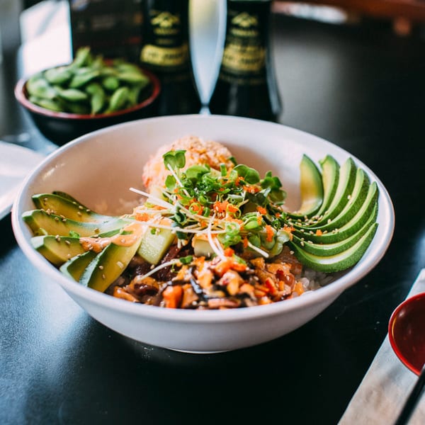 A vibrant poke bowl with sliced avocado, microgreens, and fish roe, next to edamame.