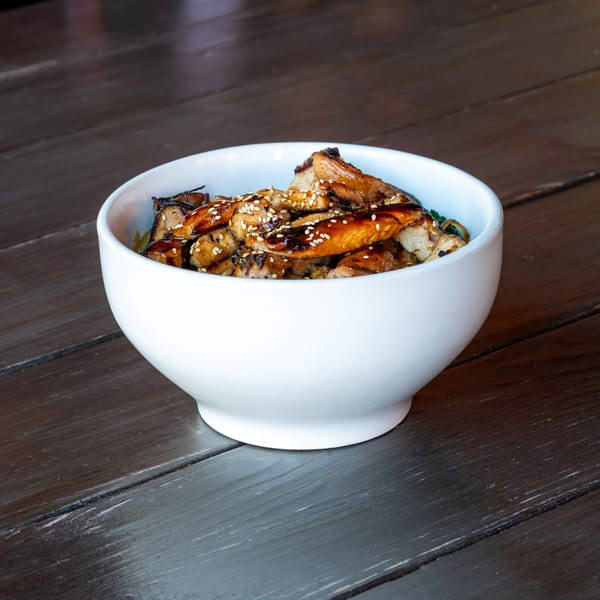 Sushi Omakase's grilled chicken teriyaki bowl with sesame seeds on a dark wooden table.
