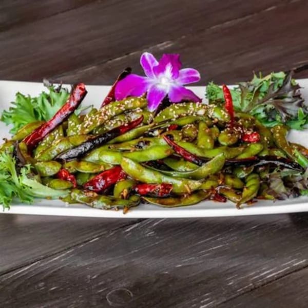 Spicy edamame with red chili peppers and sesame seeds, garnished with a purple orchid.